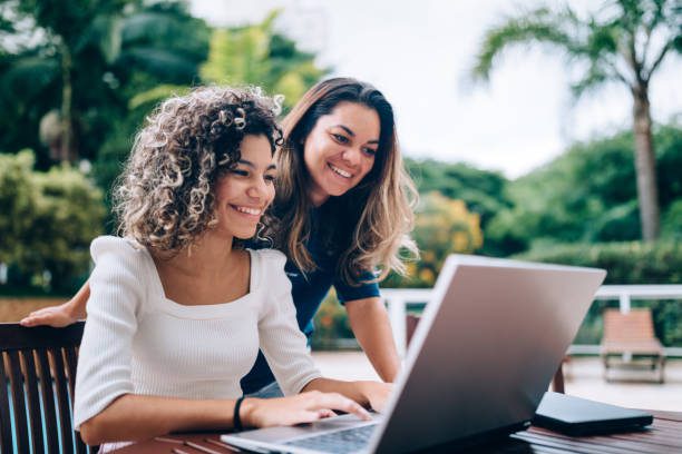 Mother and daughter using laptop at swimming pool area